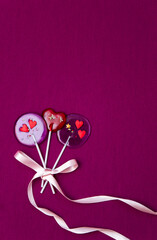 Lollipop hearts with ribbons on a bright pink background. Vertical. Copy space