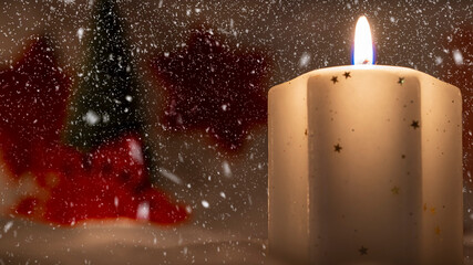 Burning white candle in snowing background witj red snowflake