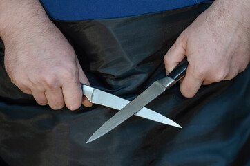 Middle-aged man holds two kitchen knives in his hands.