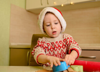 Beautiful little boy cooking Christmas cookies. Santa Claus helper
