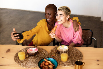 Beautiful young bestfriend females taking selfie using a smart phone and smiling while having a breakfast at home
