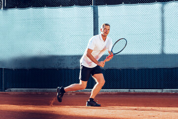 Young man plays tennis outdoors on tennis court in the morning
