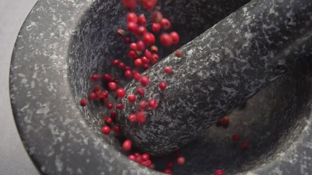 Close-up of spicy rose peppercorns falling into the grey stone mortar in slow motion