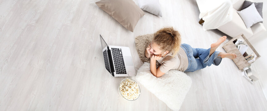 young woman lying on the floor at the computer with popcorn in living room, top view image and stay at home concept