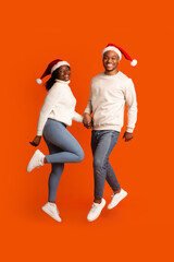 Positive Black Couple Wearing Santa Hats Jumping And Having Fun Together