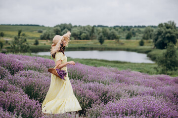 Beautiful carefree woman in dress and hat with a basket of flowers in a field of fragrant lavender. Soft selective focus, art noise