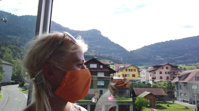 girl with surgical mask for Covid-19 Coronavirus epidemic in train of Rigi Mountain railways. Scenic landscape between Alps, valleys of Rigi Mountain railways and blue cog train by the window.