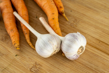 assorted vegetables a pair of large white head of garlic on a background of carrots on a wooden cutting board
