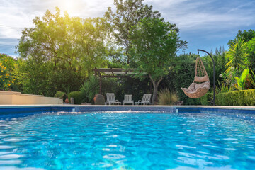 Luxurious pool in the garden of a private villa, hanging chair with pillows for leisure tourists, in summer. Portugal, Algarve.
