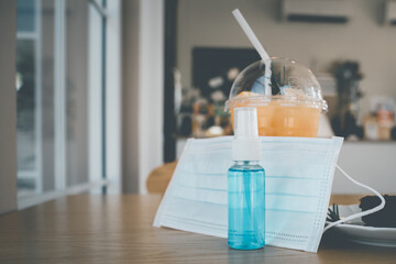 bottle of blue alcohol spray and surgical mask with blurred beverage in coffee shop , necessary for...