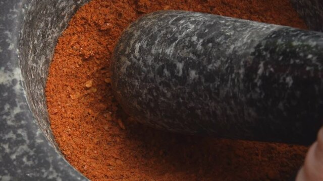 Close-up of the pestle grinding a mix of spices, peppers and sea salt in the grey stone mortar