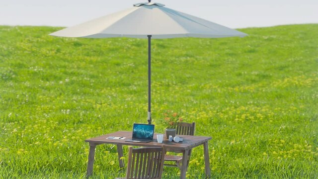 広々とした草原に置かれたウッドテーブルとノートPCの3Dモーショングラフィックス / ドローン空撮風の上昇・俯瞰アングル / ワーケーション・リゾートワークのコンセプトイメージ