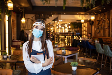 Fototapeta na wymiar Female waitress wearing protective face mask and visor while holding touchpad and reopening sidewalk cafe during COVID-19 epidemic. New normal restaurant concept.