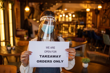 Barista holding  sign we’re open for takeaway orders only in front of restaurant. Social distancing concept when coronavirus is outbreak in city.