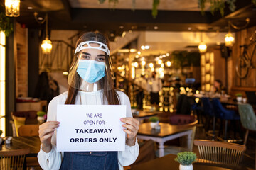 Female waitress hanging open sign while reopening restaurant for delivery and takeaway only during coronavirus epidemic.  Woman holding sign we’re open for takeaway orders only infront of restaurant.