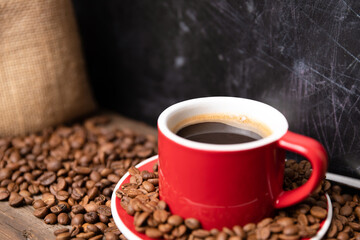 Red cup of coffee with coffee beans on dark textured background. Morning fresh energy concept.