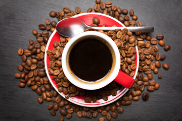 Red cup of coffee with coffee beans on dark textured background. Morning fresh energy concept.