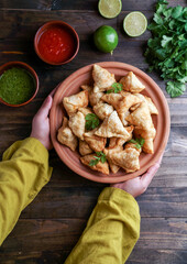 Samosa - fried/baked pastry with savoury filling, popular Indian snacks, served in bowl with spices and fresh cilantro on rustic background