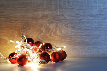 Christmas and New Year template from red shiny, sparkling, matte christmas balls illuminated by a led garland on light oak wood textured surface with copy space