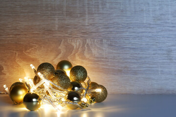 Christmas and New Year template from gold shiny, sparkling, matte christmas balls illuminated by a led garland on light oak wood textured surface with copy space