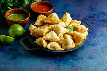 Samosa - fried/baked pastry with savoury filling, popular Indian snacks, served in bowl with spices and fresh cilantro on rustic background