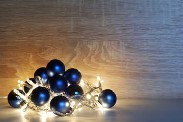Christmas and New Year template from blue shiny, sparkling, matte christmas balls illuminated by a led garland on light oak wood textured surface with copy space