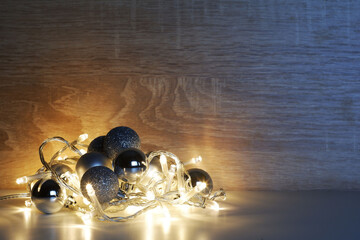 Christmas and New Year template from silver shiny, sparkling, matte christmas balls illuminated by a led garland on light oak wood textured surface with copy space