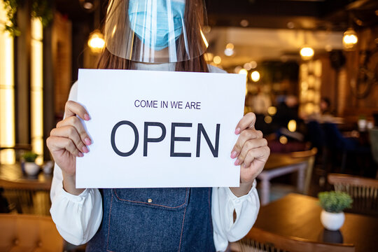 Small business owner smiling while turning the sign for the reopening of the place after the quarantine due to covid-19. Happy businesswoman standing at her restaurant or coffee shop