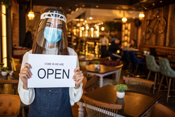 Cafe opening after lockdown. Open sign on front door of restaurant or grocery store. Waiter in apron greeting customer. Welcome message on bakery entrance. Back to work after quarantine.