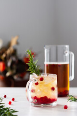 Cold refreshing black tea with ice and cranberries, jug and glass with berries and tea decorated with a sprig of rosemary on a white wooden background