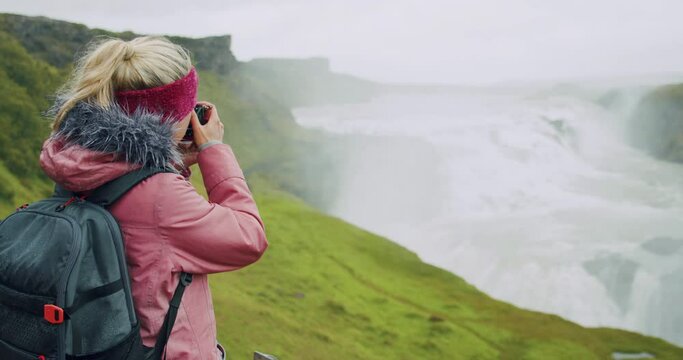 Tourist woman with backpack capture the Gullfoss waterfall with her camera. Famous attraction and landmark destination on Iceland on the Golden Circle