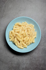White fusilli pasta cooked and served on a blue plate on a grey background