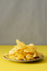 Crispy chips on a gray plate on a yellow table against a gray wall background, trendy colors of the year