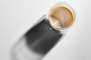 Glass cup of coffee on white surface with long shadow