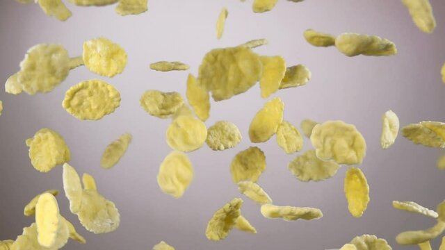 Cereal corn flakes are flying up and rotating on the white background in the slow motion