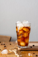 Cold refreshing iced coffee in a glass on a wooden board close-up, cocoa beans are scattered on the table
