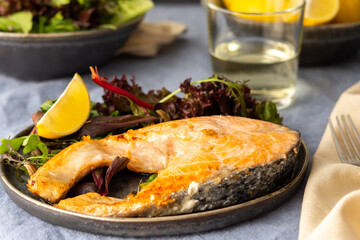 Fried salmon steak with salad in a plate , white wine in a glass, delicious hearty dinner or lunch