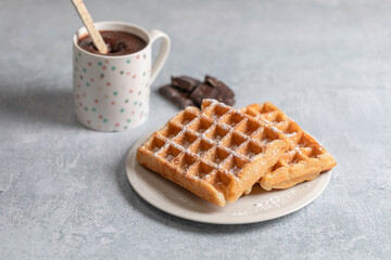 Two homemade waffles with a cup of hot chocolate over a white table.