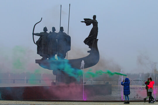 Kyiv, Ukraine-December 05, 2020:Monument of the founders of Kyiv after reconstruction in the colorful smoke. Kyi, Shchek, Horyv and Lybid in the boat on the bank of the Dnieper River. Winter foggy day