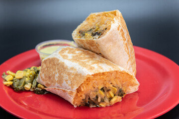 Veggie burrito loaded with fresh vegetables cut in half and presented on a red plate.