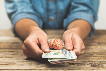Hands hold money and a brain. Making money with your intellect. Investing money in education.