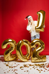 cheerful caucasian young woman in white sweater, blue jeans and red christmas hat thinks about something, picture isolated on red background