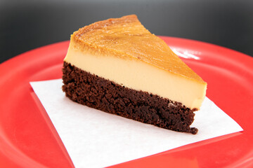 Chocolate layer on bottom of Mexican Flan dessert cut into a wedge and presented on a red plate.
