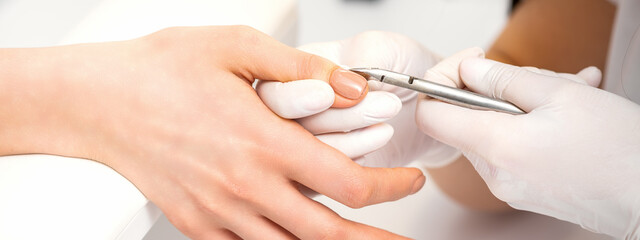 Manicure master is removing cuticles with a nail clipper in a nail salon - obrazy, fototapety, plakaty