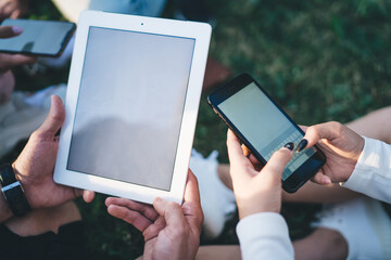 Faceless couple using tablet and phone on park meadow