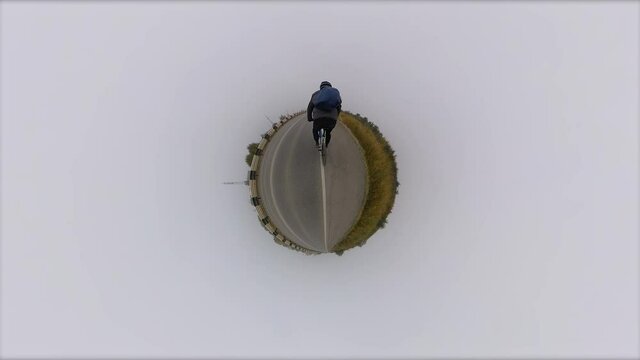 Bicycling. Tiny planet. 360 degree camera.
The cyclist rides along the road. There is fog around him. Autumn.