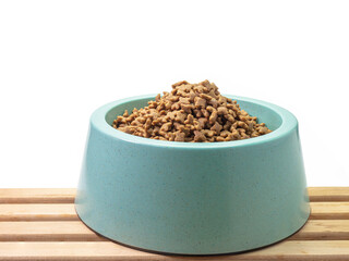 The close up of dry dog treat food in blue green plastic dog bowl, pet equipment with wood plank on white background.