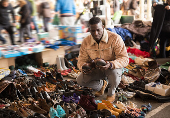 ordinary african american guy sells sacond hands shoes at flea market