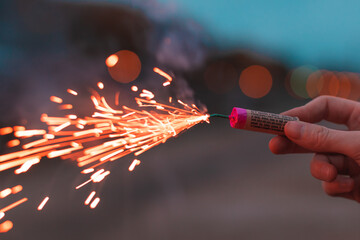 Young Man Lighting Up Firecracker in his Hand Outdoors in Evening. Guy Getting Ready for New Year Fun with Fireworks or Pyrotechnic Products - CloseUp Shot