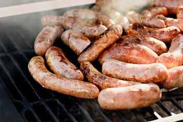 Grilled sausages or bratwurst on grill with smoke and flame. Delicious german sausages on barbecue grill. summer picnic, close up of grill, concept of resting in fresh air. BBQ in garden.
